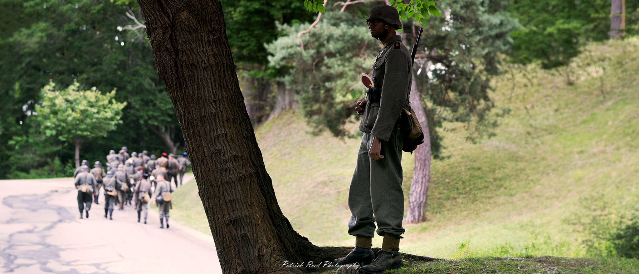 A German soldier observing troop movements from a vantage point, carefully assessing the situation. The image highlights the strategic role of the soldier, with a focus on his attentive posture and the dynamic nature of military operations.